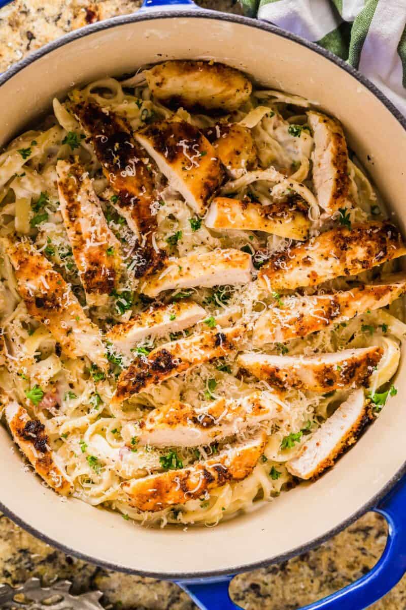 Sliced chicken is placed on top of cooked noodles in a pan.