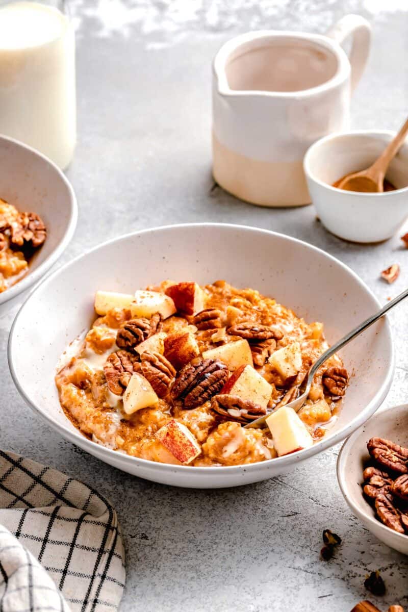 apple cinnamon oats with cubed apples and pecans in a white bowl and spoon