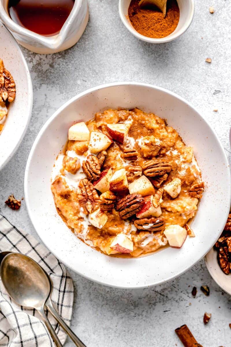 a closer overhead shot of white bowl with apple cinnamon oats and toppings (pecans and fresh apples)