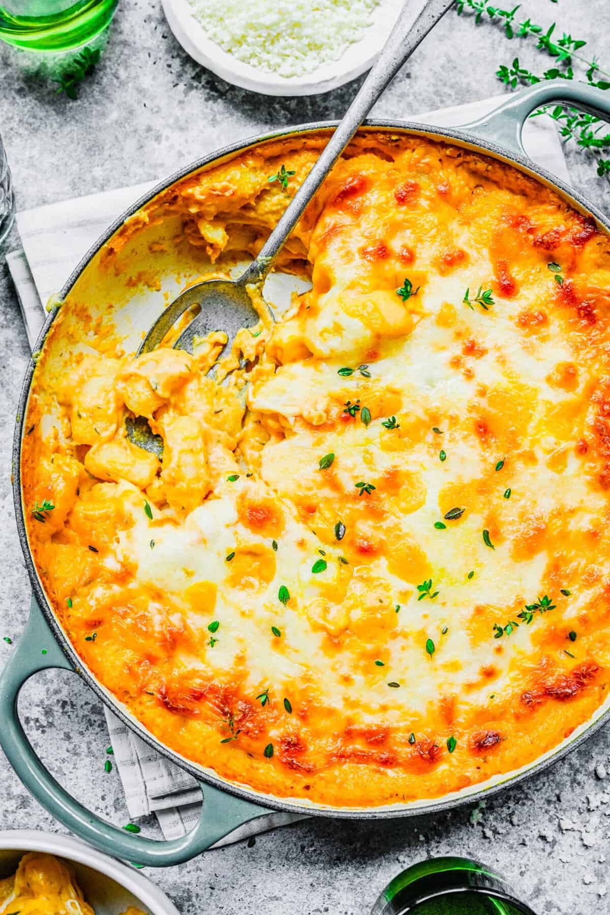 Overhead view of baked pumpkin gnocchi in a pot, with a serving spoon, and a spoonful missing