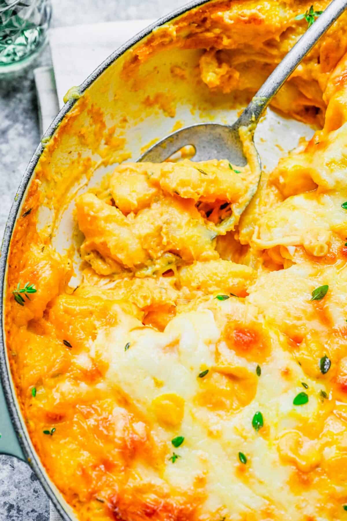 Close up of baked pumpkin gnocchi in a pot, with a serving spoon, and a serving missing