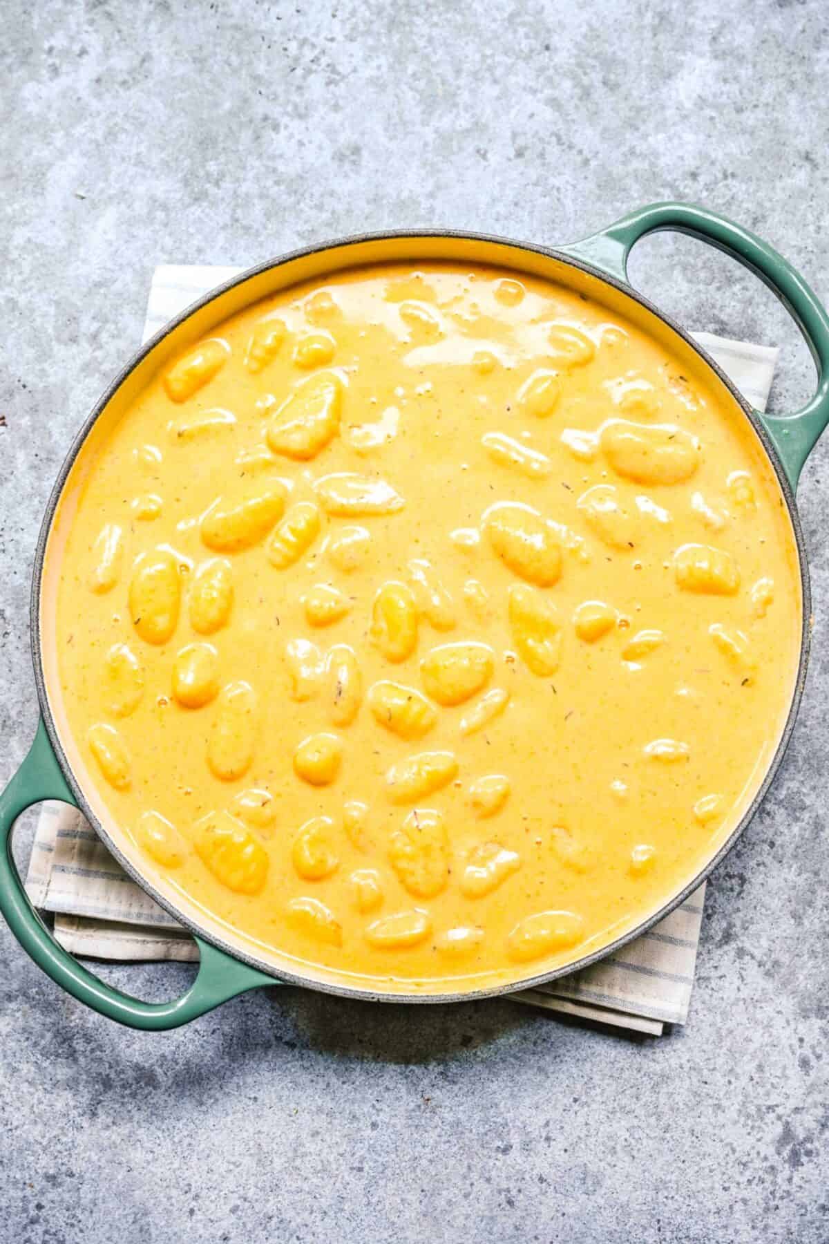 A baking dish filled with unbaked gnocchi in pumpkin sauce, on a kitchen towel