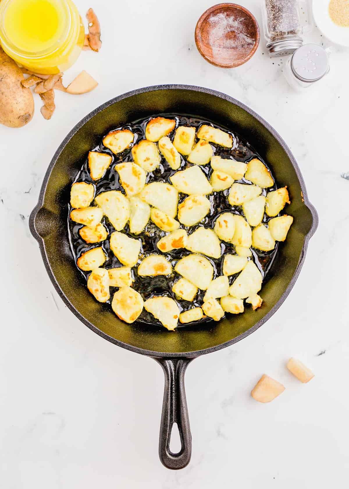 overhead shot of potatoes being cooked in a cast iron skillet with duck fat