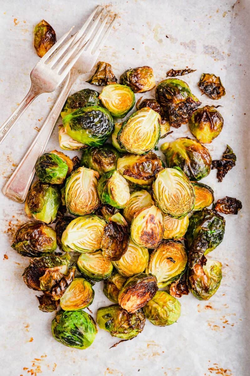 overhead shot of roasted garlic sprouts on a baking sheet with parchment paper and forks.