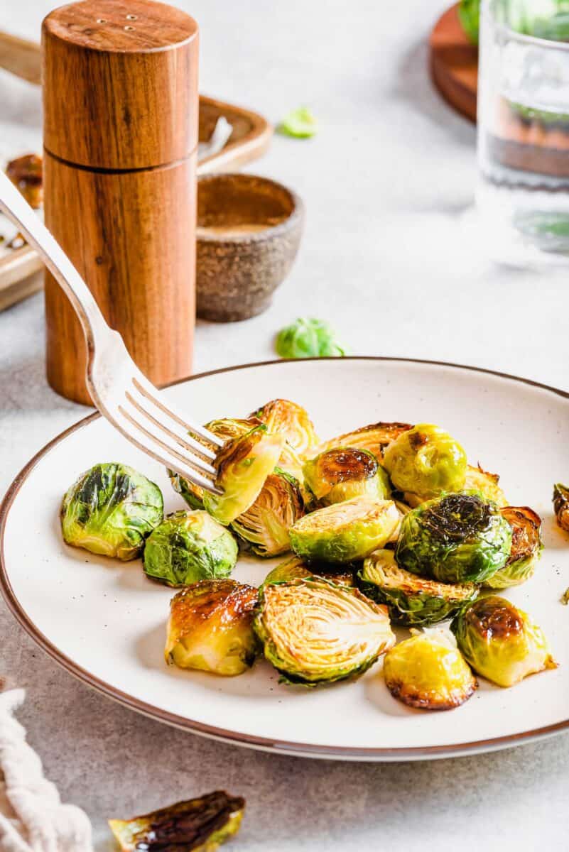 roasted brussels sprouts on a white plate with a brown rim. a brussels sprout is on the end of a fork.