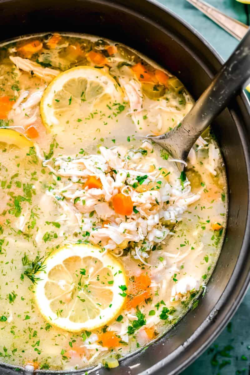 up close shot of lemon chicken and rice soup in a ladle in the pot with lemon slices around the ladle