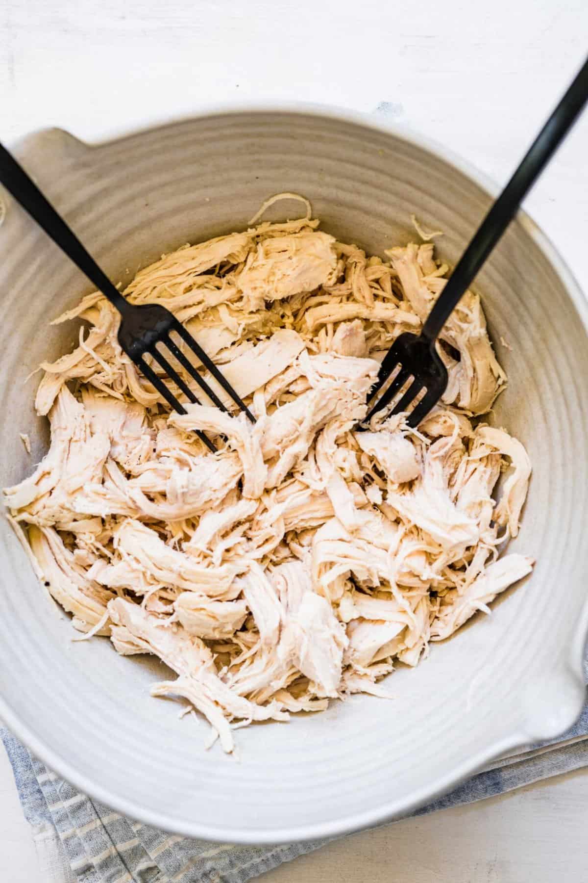 two black forks in a large bowl of shredded chicken