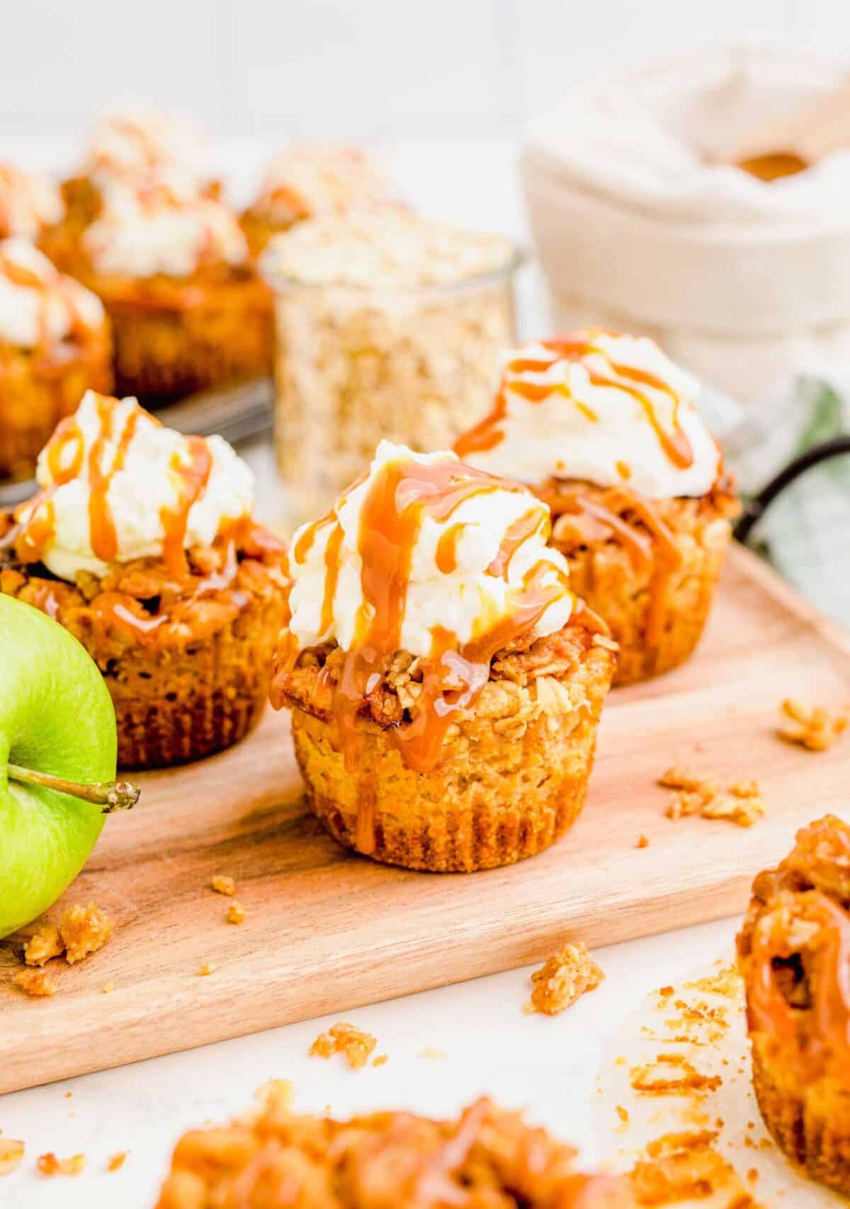 Close up of three caramel apple cheesecakes, next to an apple, with a jar of oats in the back