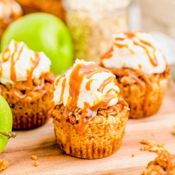 Close up of three caramel apple cheesecakes, with an apple and a jar of oats in the background