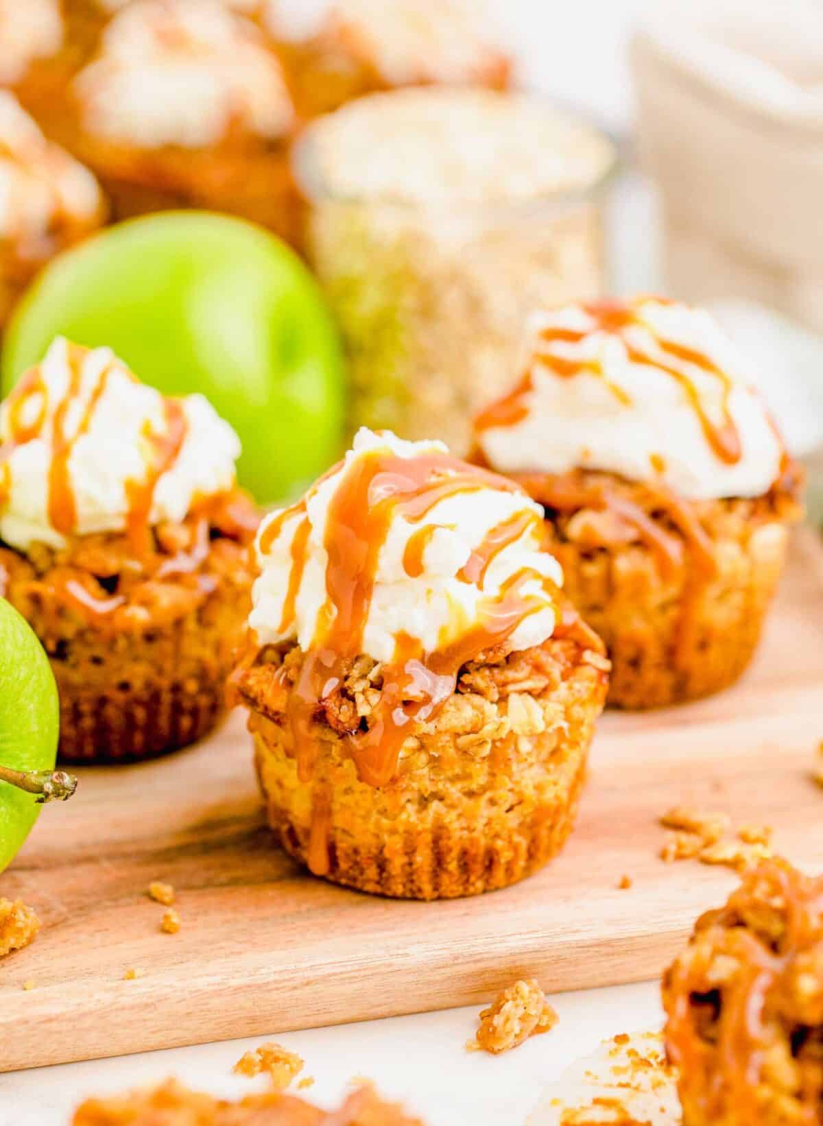 Close up of three caramel apple cheesecakes, with an apple and a jar of oats in the background