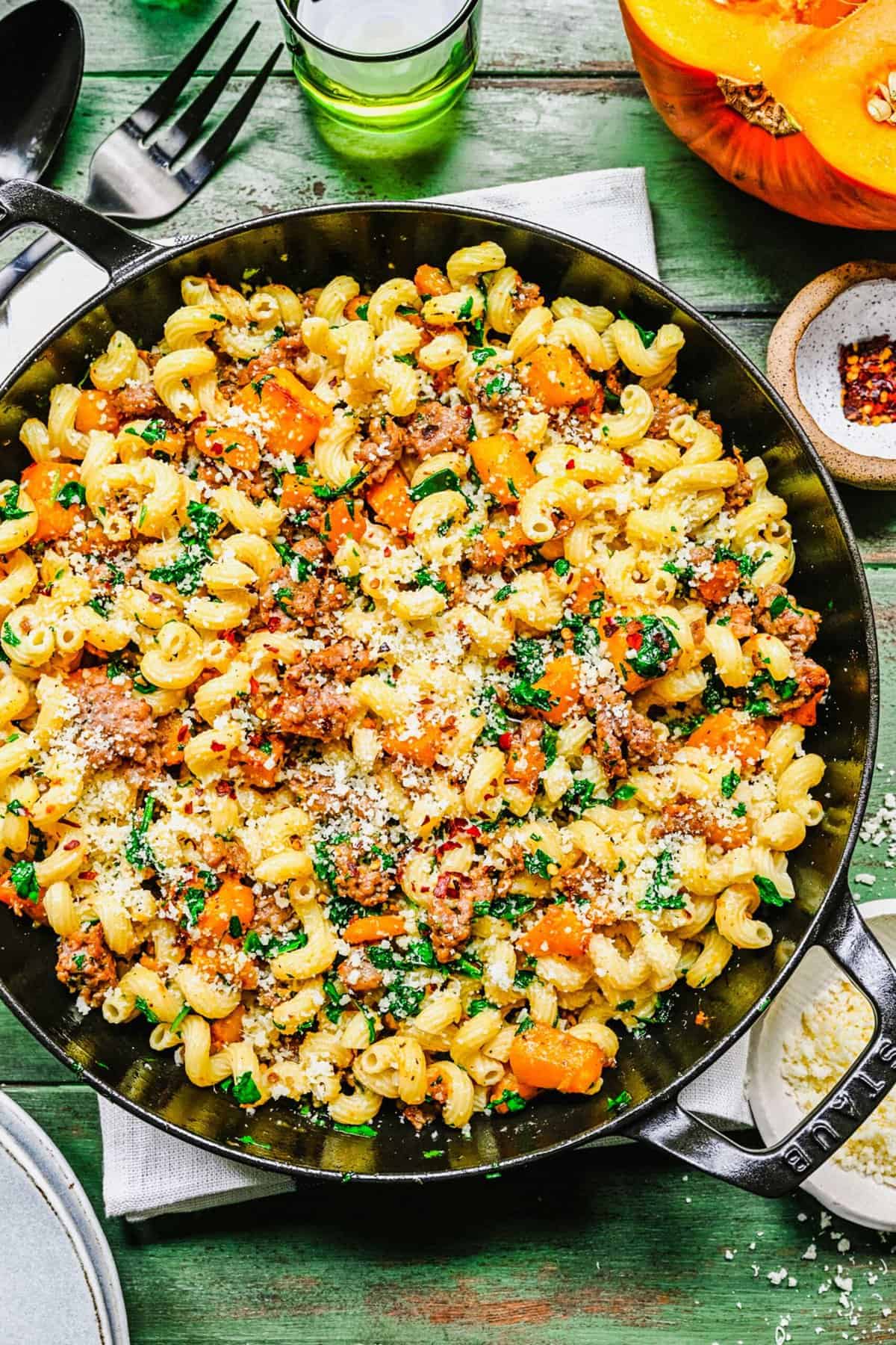 overhead shot of finished pasta with pumpkin and sausage in a staub cast iron pot with parmesan cheese and red pepper flakes sprinkled on top