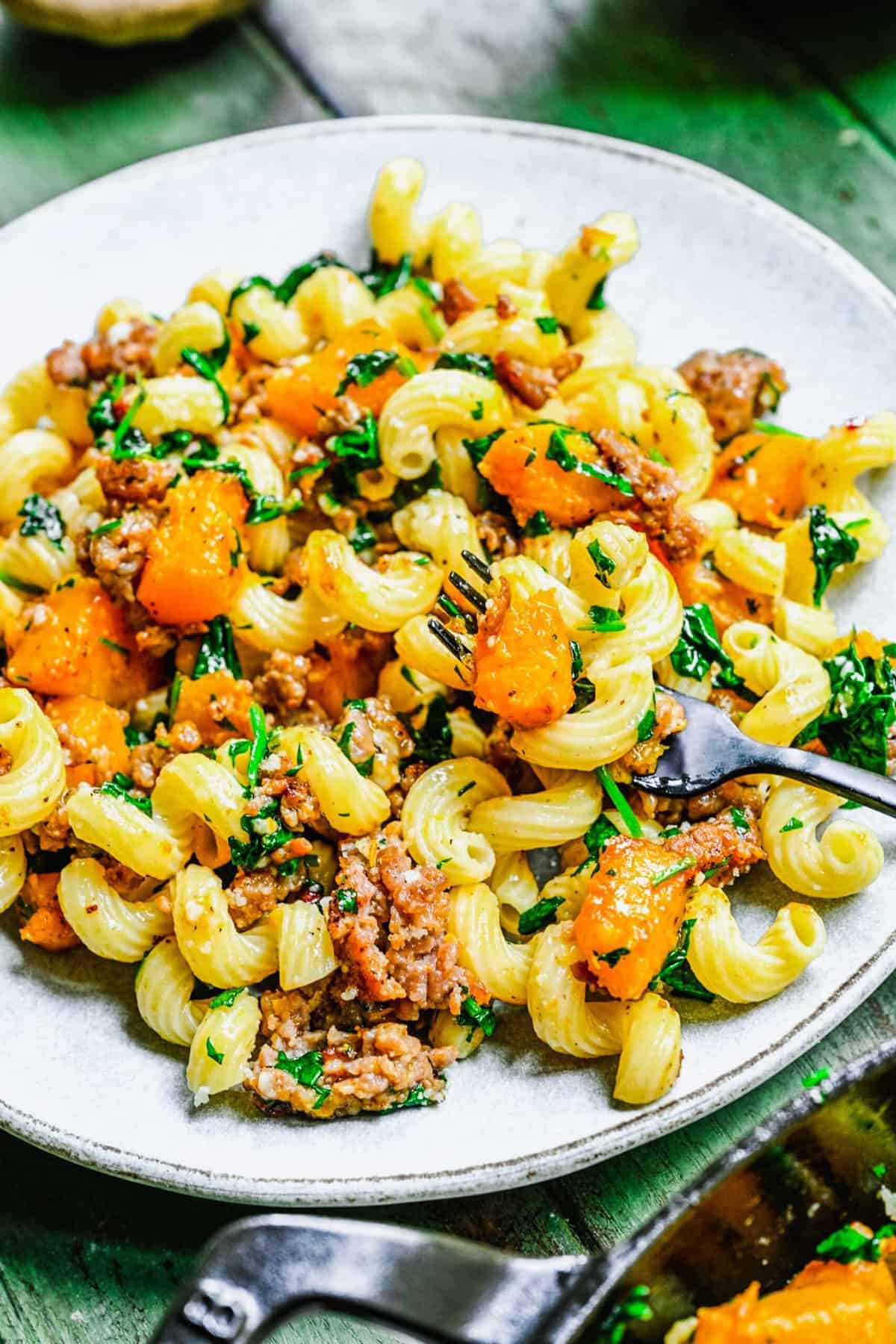 pasta with pumpkin and sausage plated on a grey ceramic plate with a fork that has some pasta and pumpkin on it