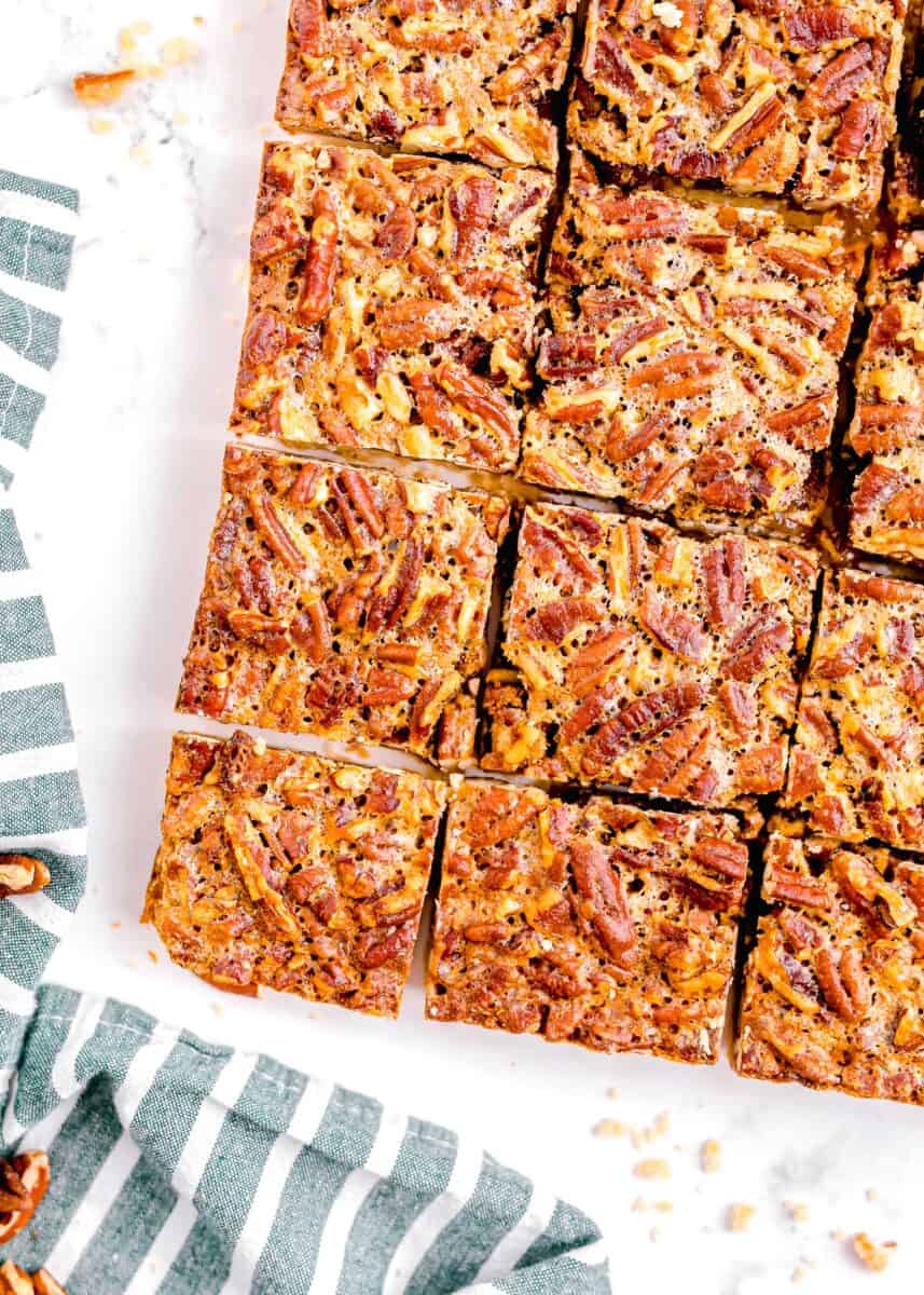 overhead shot of pecan pie bars cut into squares on a white background with a blue and white striped linen towel