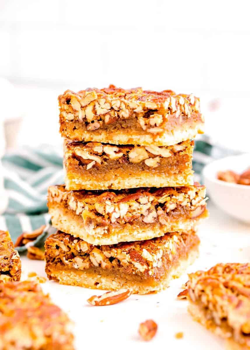five pecan pie bars stacked on top of each other surrounded by other pecan pie squares and a green and white striped linen