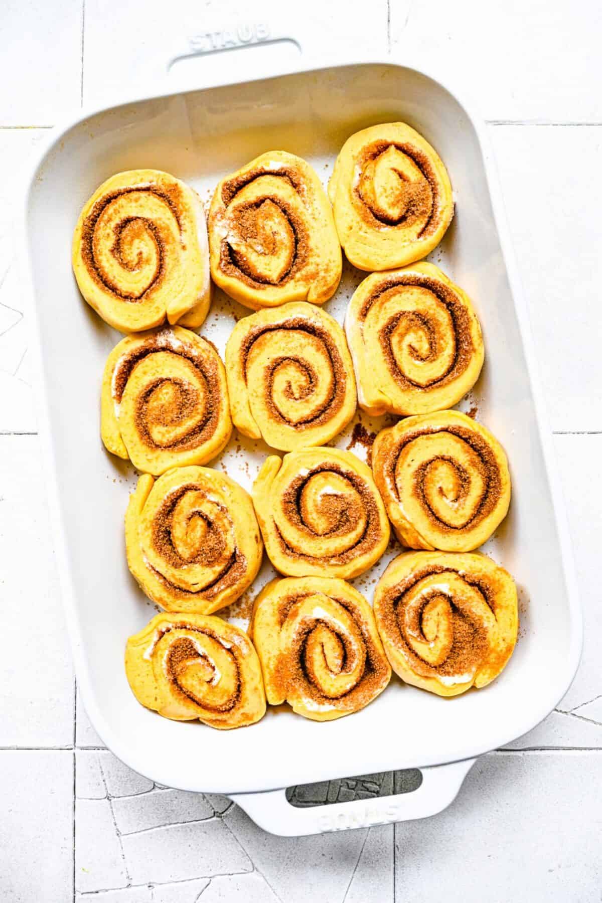 Overhead view of a baking tray with 12 unbaked pumpkin cinnamon rolls