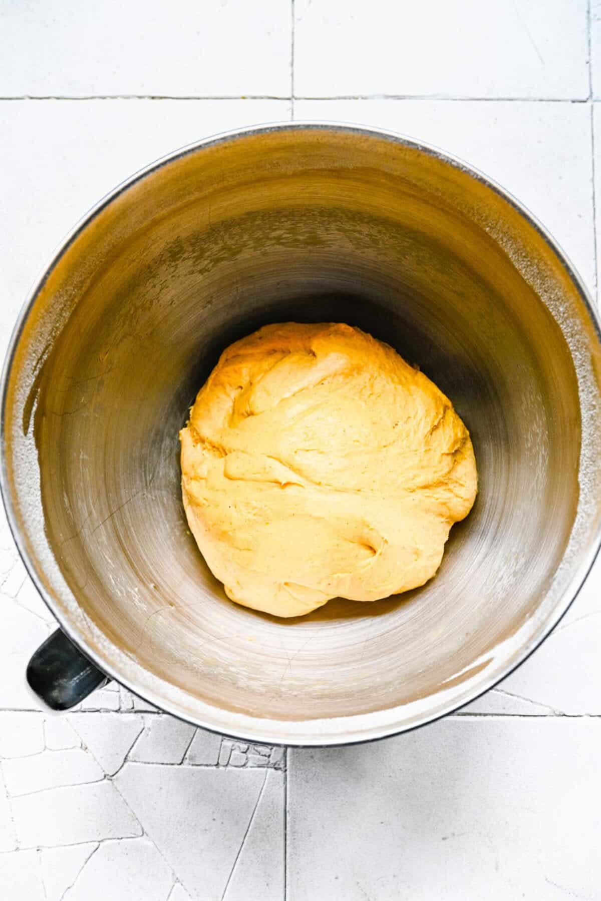 A stand mixer bowl with a ball of pumpkin cinnamon roll dough