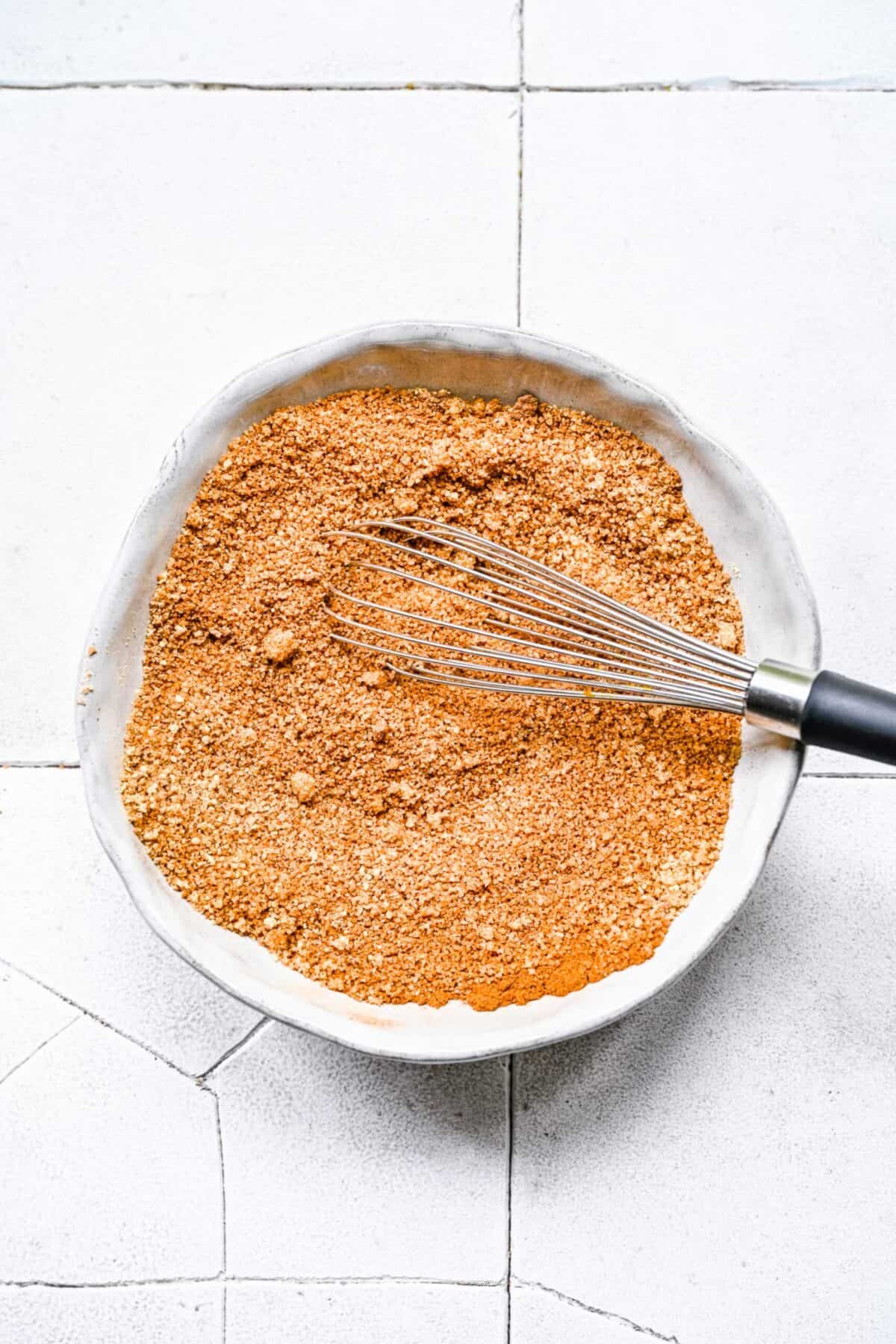 A bowl with cinnamon roll spice mixture, mixed together, with a whisk in it
