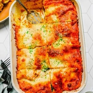 A baking tray with pumpkin lasagna cut into eight slices, with one slice removed and a serving spoon in it