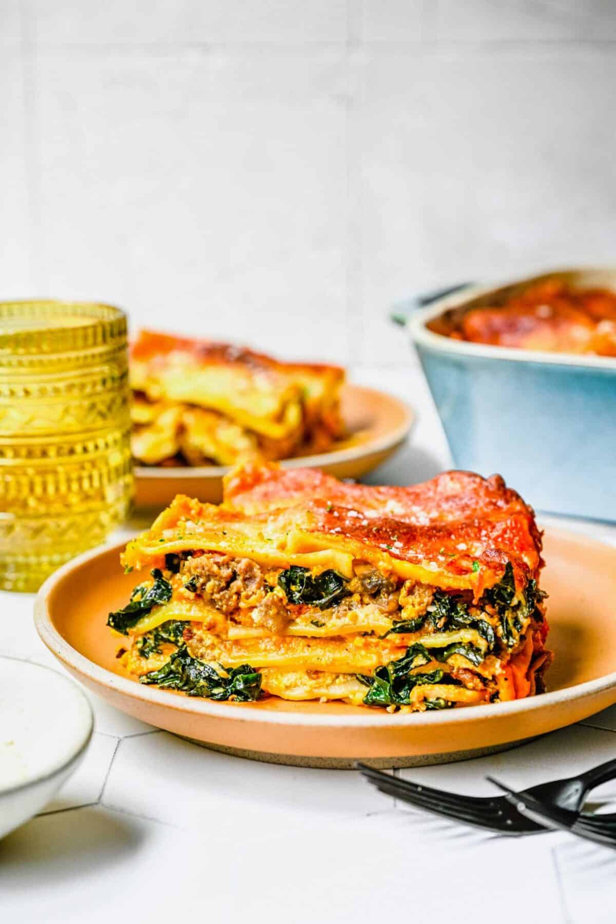 A slice of pumpkin lasagna on a plate, with another slice and a baking dish in the background