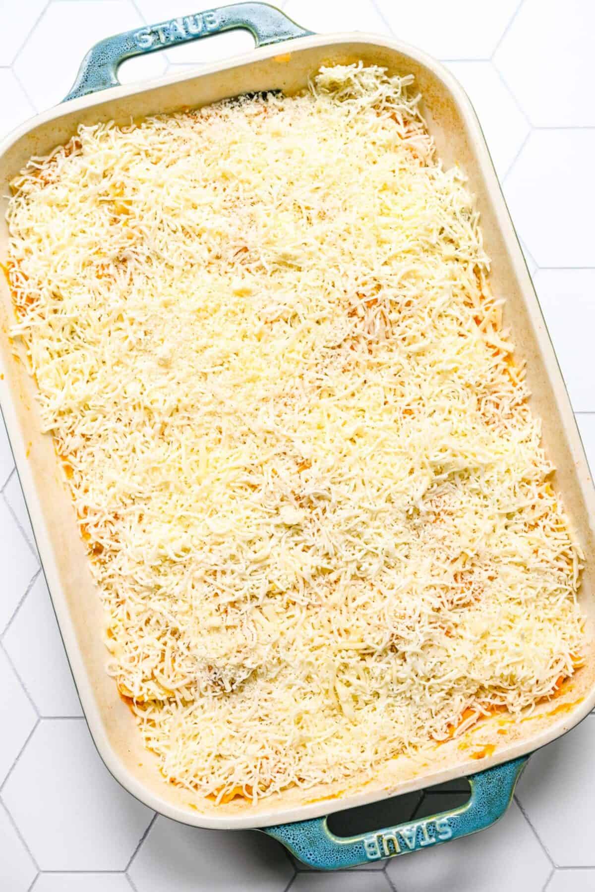 A baking dish filled with an uncooked pumpkin lasagna, topped with shredded mozzarella and parmesan cheese