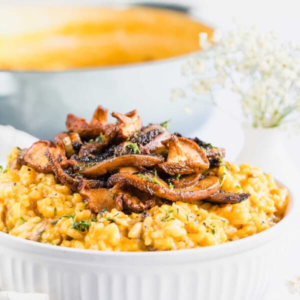 A casserole dish of risotto with mushrooms on top, with a pot in the background and a fork in the foreground