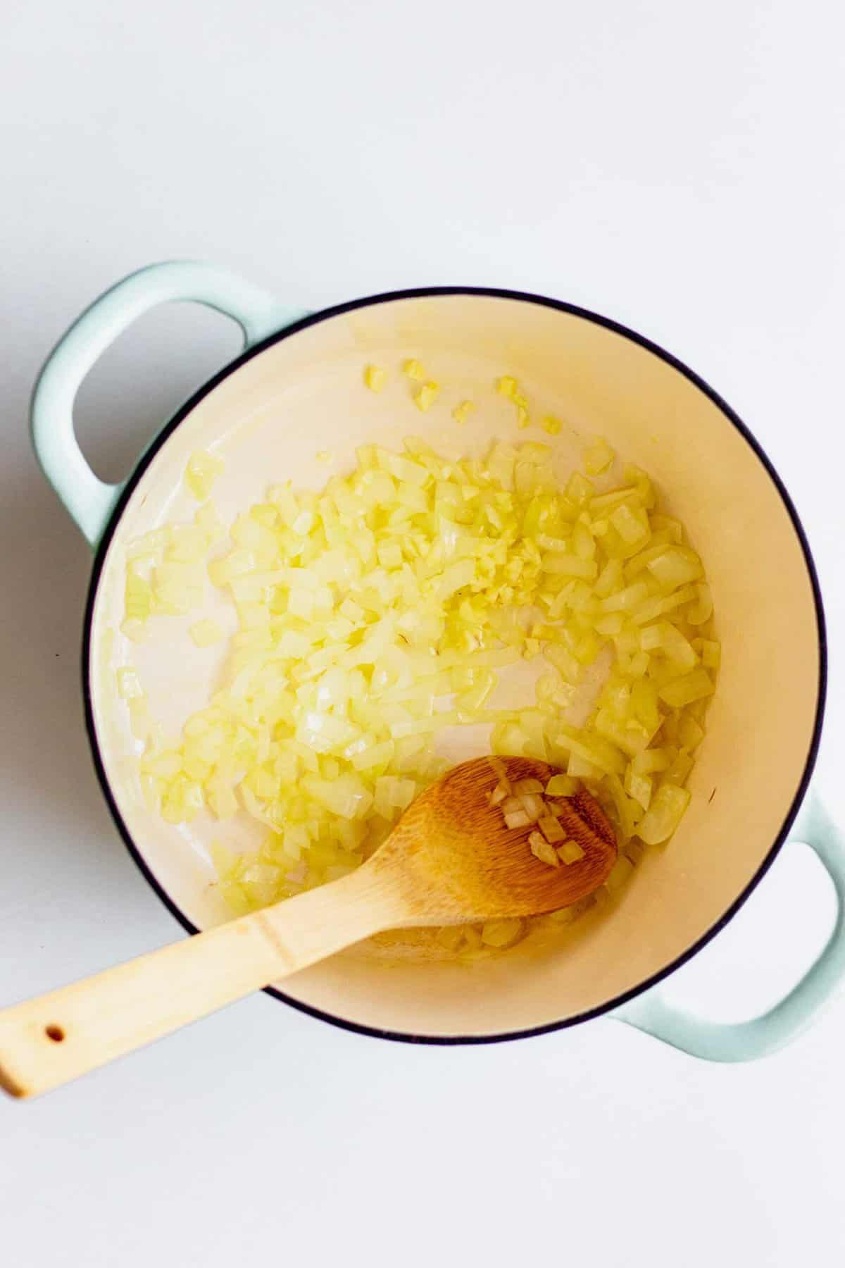 Sautéing onions and garlic in a large pot with a wooden spoon