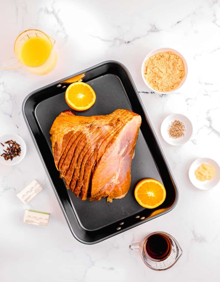 overhead image of baked glazed ham: spiral ham, brown sugar, dijon mustard, maple syrup, butter, cloves, and orange juice