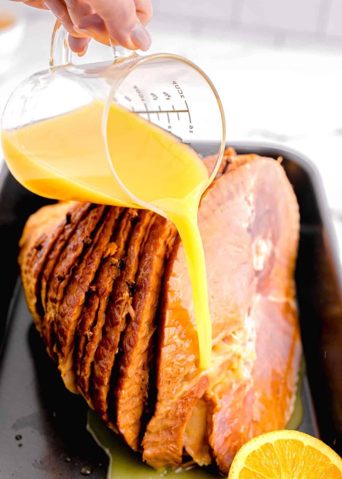 pouring orange juice on top of spiral ham in roasting pan