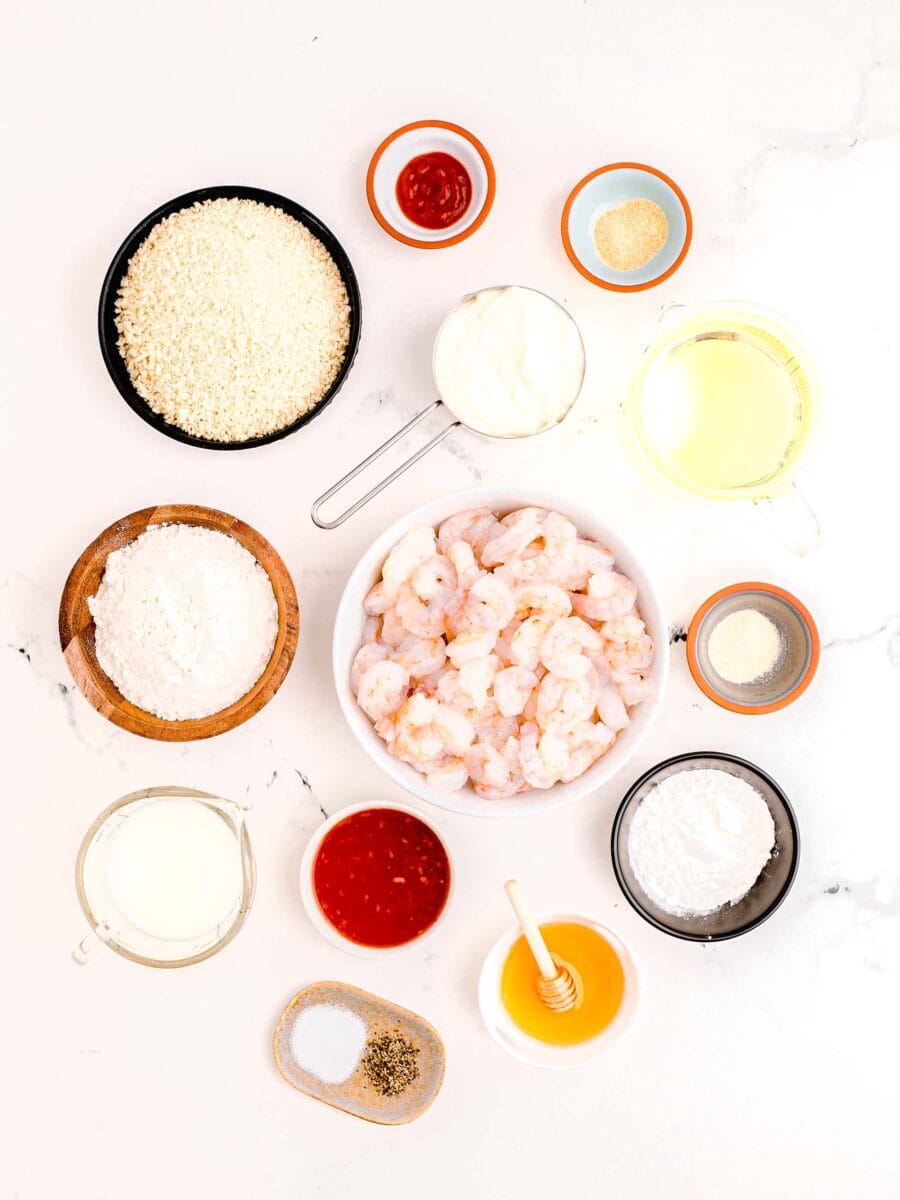 overhead image of bang bang shrimp ingredients: sriracha, garlic powder, oil, onion powder, cornstarch, honey, salt and pepper, sweet chili sauce, buttermilk, flour, panko breadcrumbs, mayo and raw shrimp