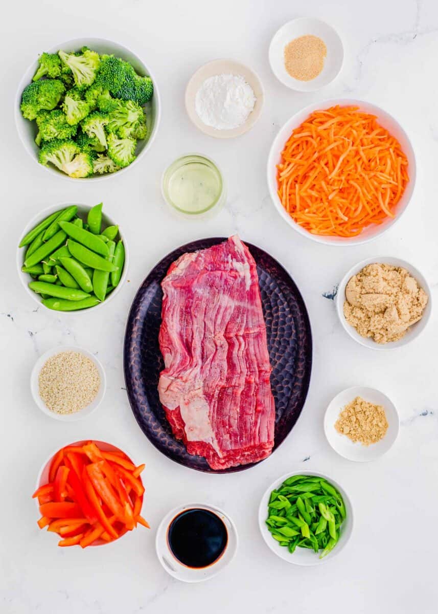 overhead image of ingredients for beef stir fry: broccoli, cornstarch, garlic powder, carrots, brown sugar, ground ginger, scallions, soy sauce, red bell peppers, sesame seeds, sugar snap peas, and vegetable oil