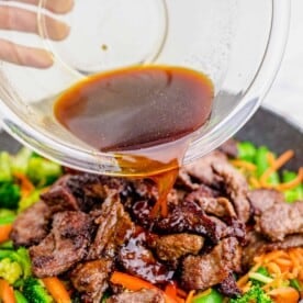 sauce is being poured on top of the browned beef slices and cooked vegetables in a grey nonstick skillet