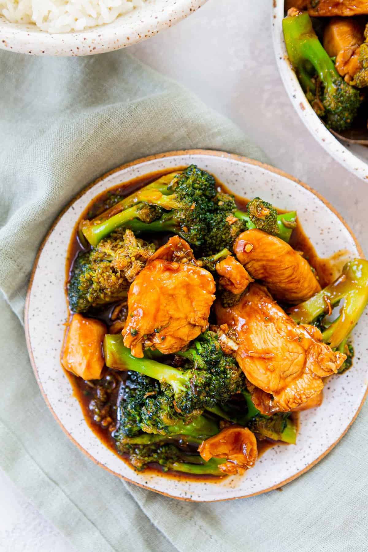 overhead image of chinese chicken and broccoli on a small plate next to rice and on a light green linen towel