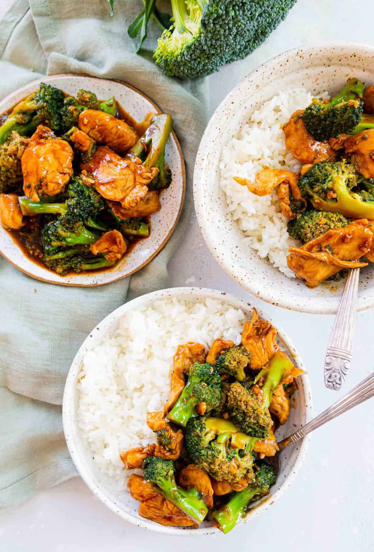 overhead image of plated chinese chicken and broccoli in bowls with rice and plates.