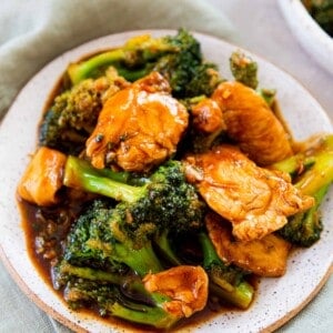 up close image of chinese chicken and broccoli on a ceramic plate on top of a light green linen towel