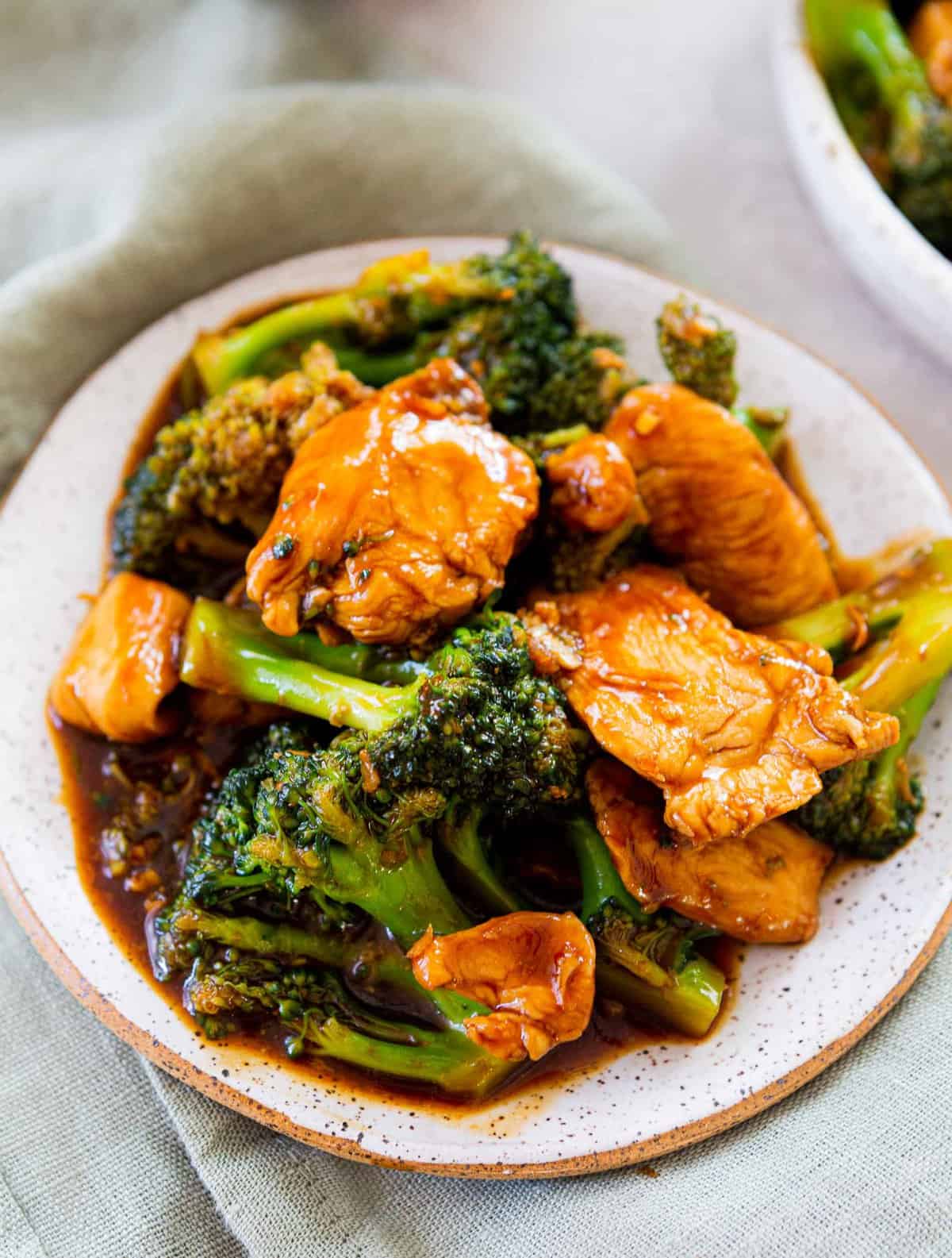 up close image of chinese chicken and broccoli on a ceramic plate on top of a light green linen towel