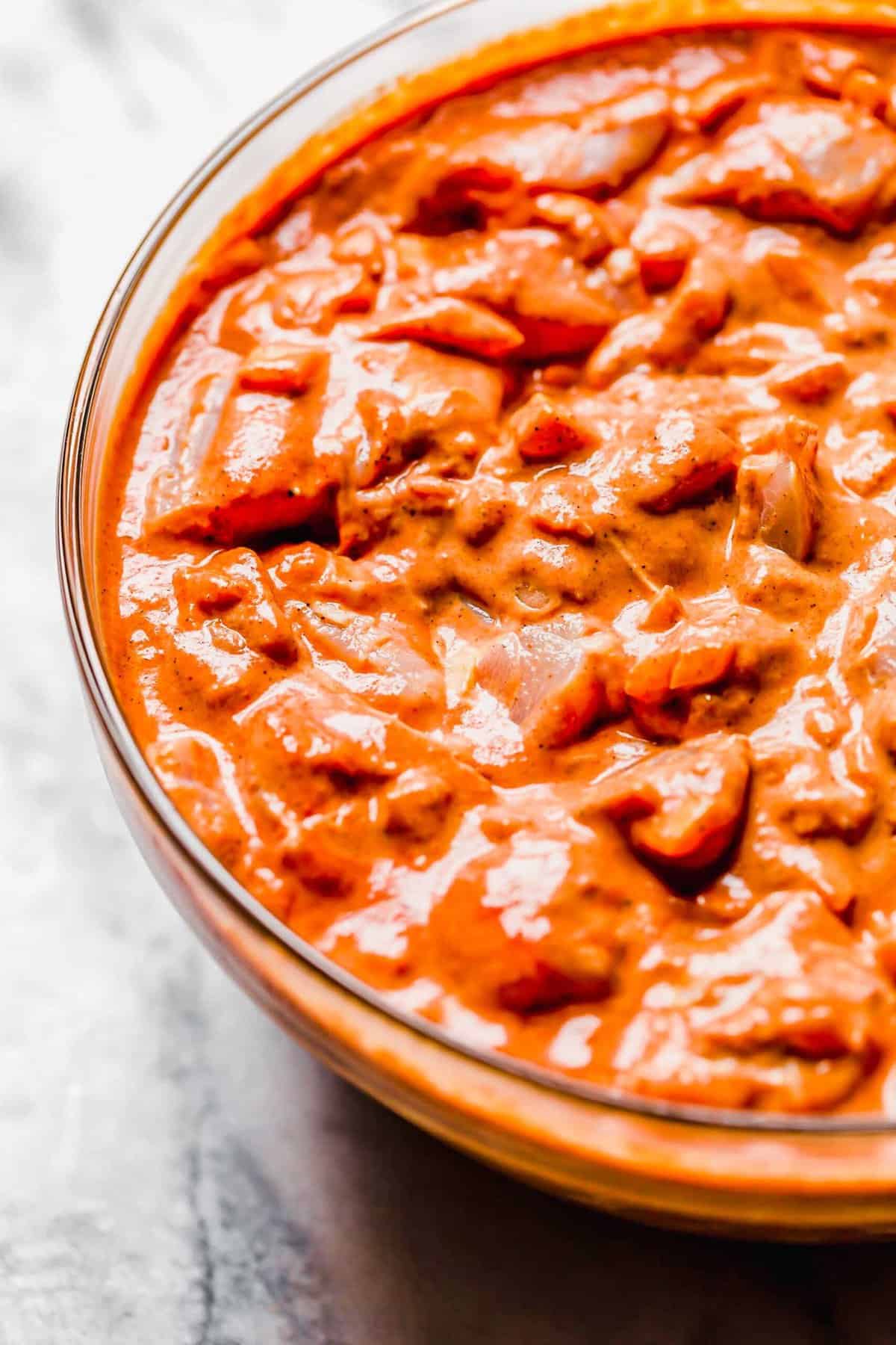 up close shot of chicken tikka masala mixture marinating in a large clear bowl