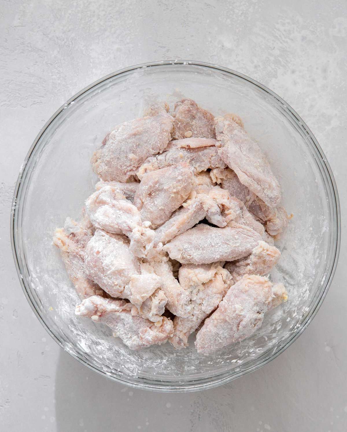 overhead image of chicken wings tossed in cornstarch in a large clear bowl