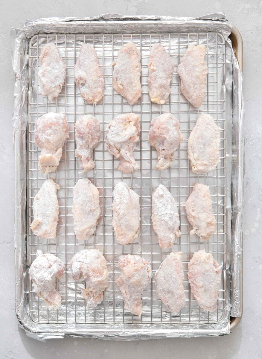 overhead image of a large baking sheet covered in foil with a stainless steel baking rack on top with chicken wings lined evenly across the baking rack