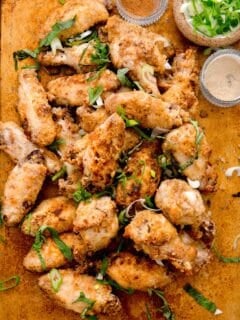 overhead image of baked and browned chinese salt and pepper chicken wings. chinese five spice powder, white pepper powder, and fresh scallions can be seen next to the pile of chicken wings