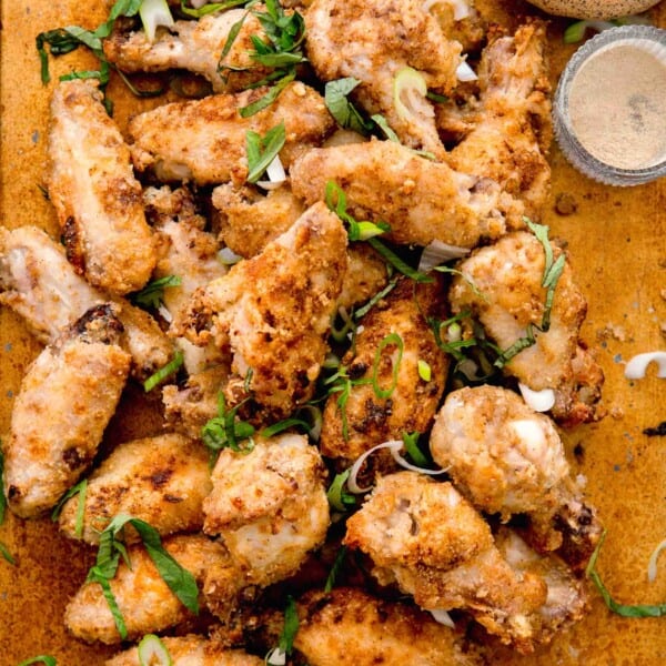 overhead image of baked and browned chinese salt and pepper chicken wings. chinese five spice powder, white pepper powder, and fresh scallions can be seen next to the pile of chicken wings