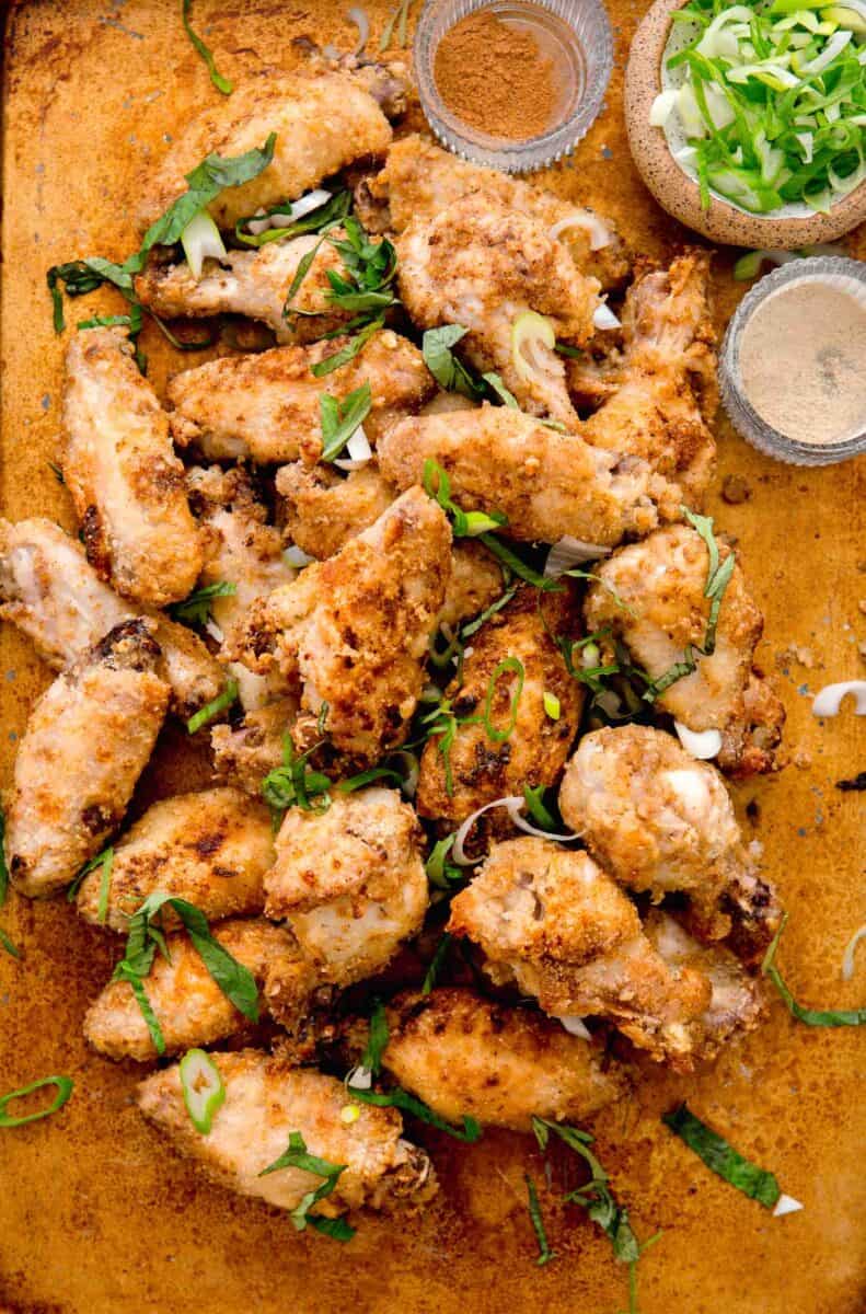 overhead image of baked and browned chinese salt and pepper chicken wings. chinese five spice powder, white pepper powder, and fresh scallions can be seen next to the pile of chicken wings