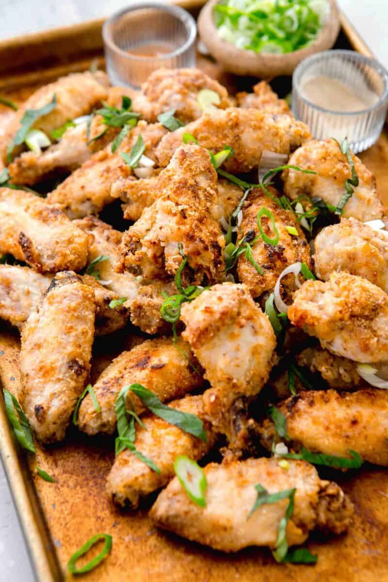 chinese salt and pepper chicken on a large baking sheet with fresh basil and scallions sprinkled on top with spices in the background