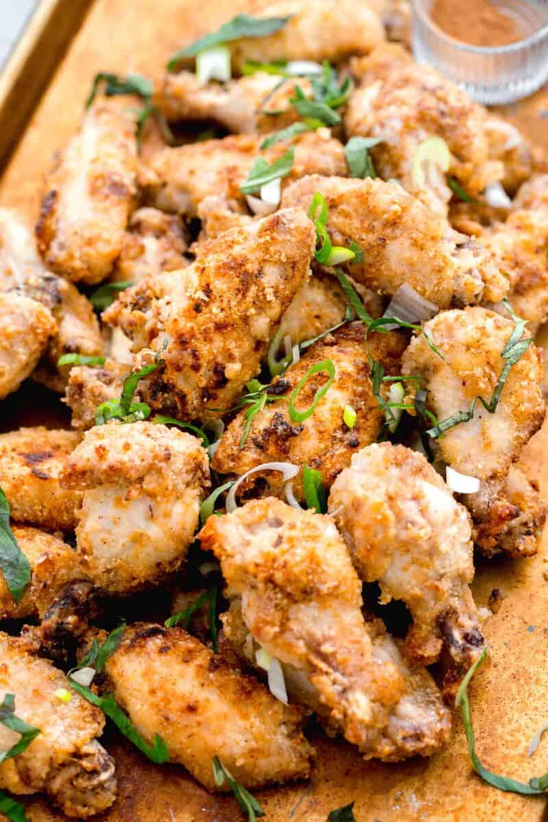 chinese salt and pepper chicken on a large baking sheet with fresh basil and scallions sprinkled on top with spices in the background