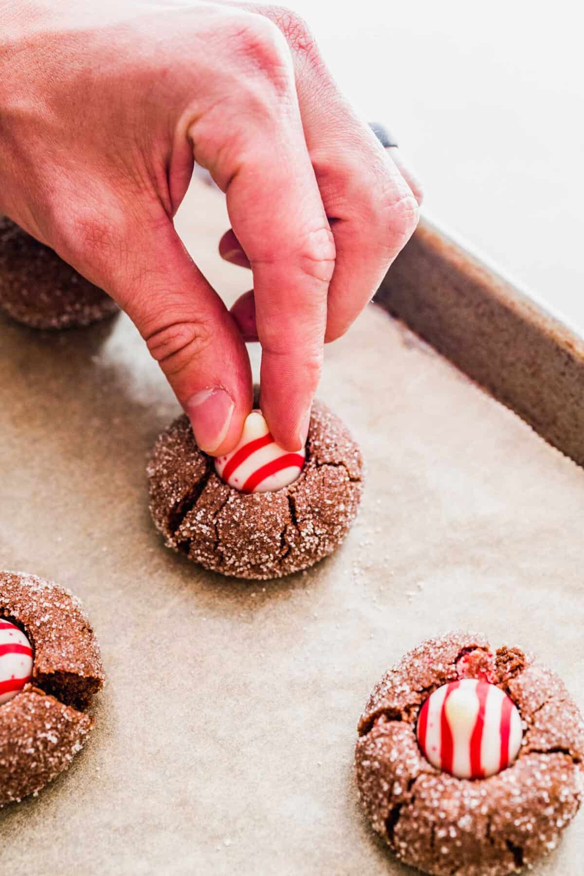 A hand pushing a Hershey's peppermint kiss into a baked chocolate peppermint kiss cookie
