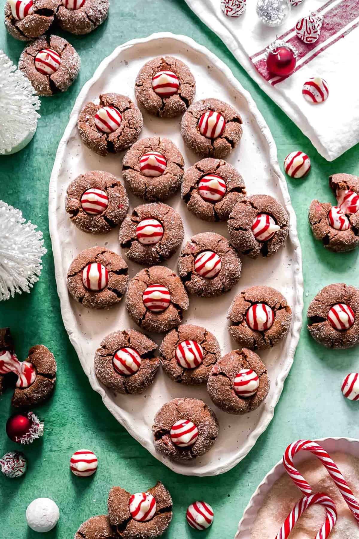 An oval tray filled with chocolate peppermint kiss cookies, surrounded by Hershey's peppermint kisses