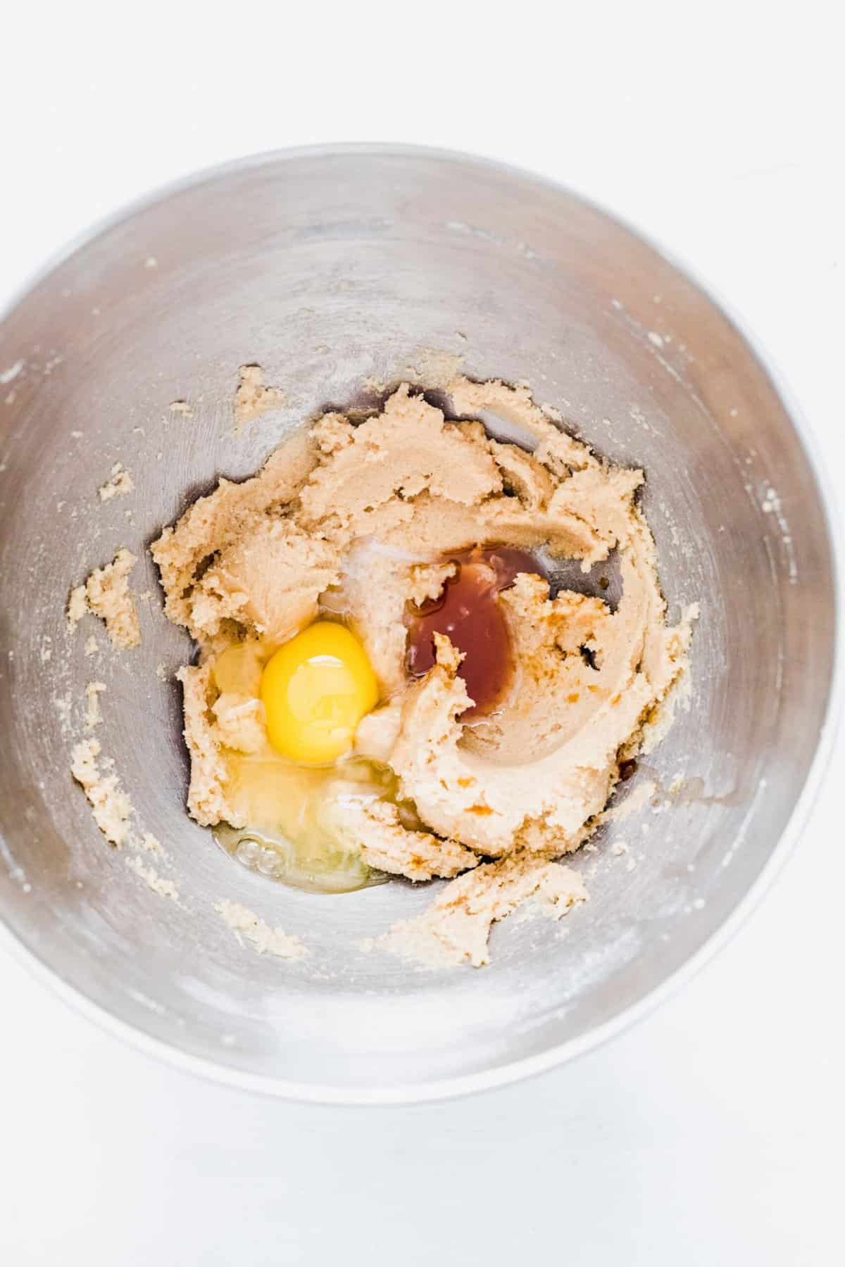 A mixing bowl with creamed butter, sugar, and brown sugar, with an egg, vanilla extract, and peppermint extract on top