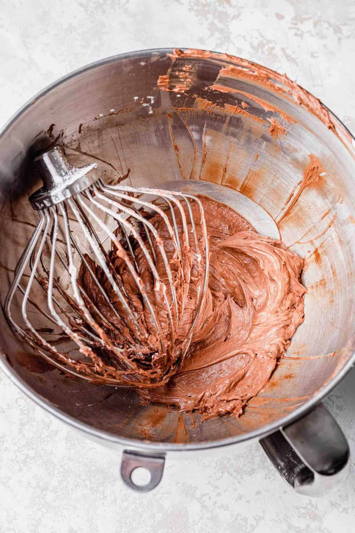A stand mixer bowl filled with chocolate peppermint frosting, with a whisk attachment in it