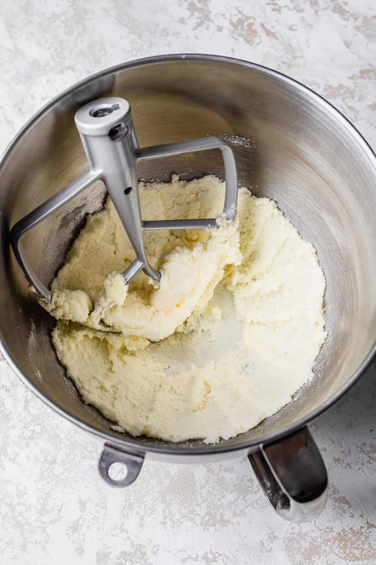 A stand mixer bowl filled with butter and cream that have been beaten, with a paddle attachment in the bowl