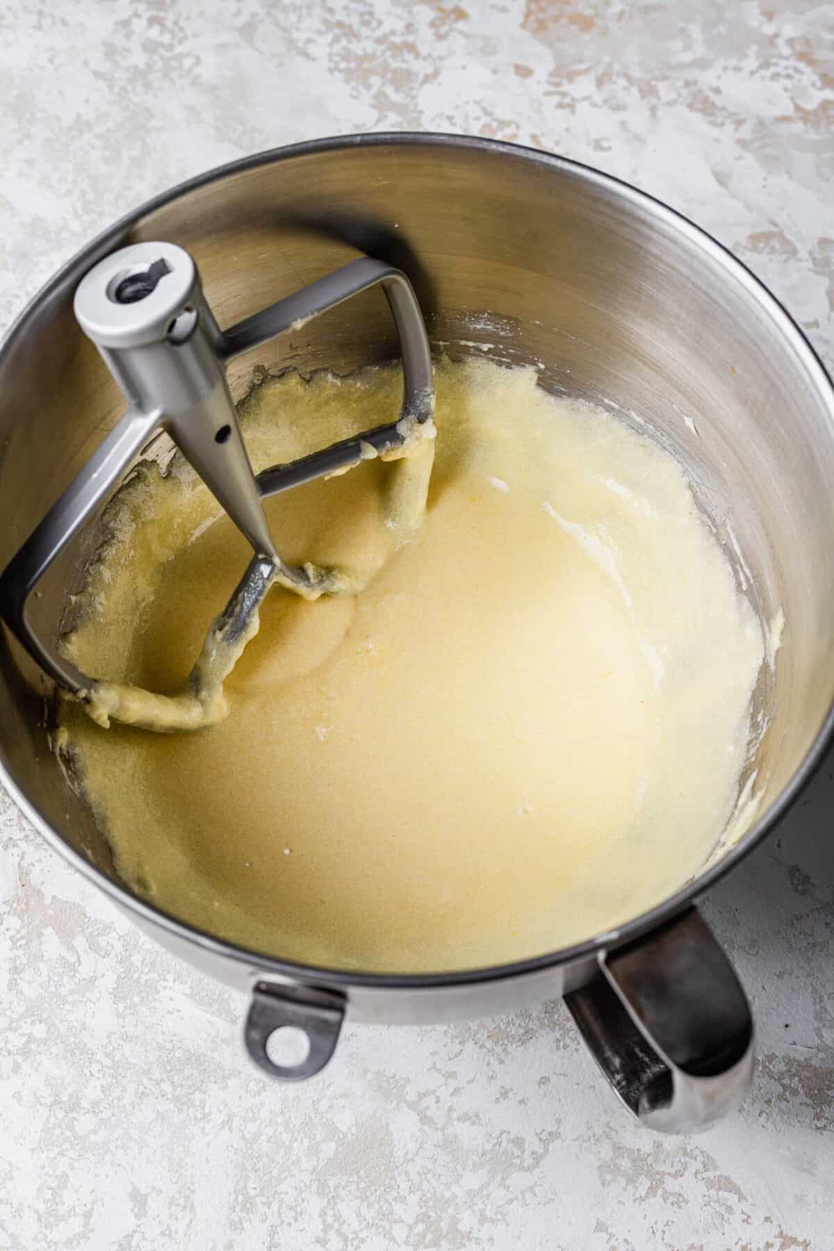 A stand mixer bowl filled with beaten butter, sugar, eggs, and sour cream, with the paddle attachment in it