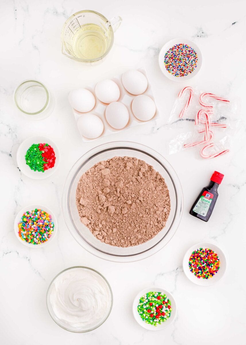 ingredients for christmas tree brownies: oil, eggs, sprinkles, candy canes, green food coloring, sprinkles, white frosting, and brownie mix